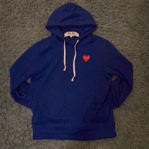 Blå hoodie CDG hoodie  - Säljer en snygg blå hoodie från CDG med en röd hjärtdetalj på bröstet.  Den är ganska liten i storleken och sitter smalt runt midjan. Den är däremot inte ”autentisk”. Kom jätte gärna med pris förslag. 