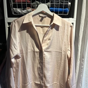 Beige blus från H&M - Säljer en stilren beige blus från H&M. Blusen har långa ärmar och knappar framtill. Perfekt för en elegant look.