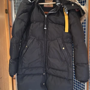 Svart long bear  från Parajumpers - Säljer en svart long bear  från Parajumpers med pälsdetaljer på huvan. Jackan har en dragkedja och knappar framtill samt praktiska fickor med knappar. Perfekt för kalla vinterdagar.