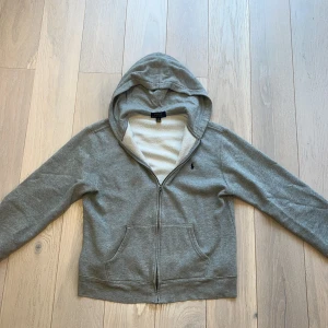 Grå hoodie från Polo Ralph Lauren - Säljer en stilren grå hoodie från Polo Ralph Lauren. Den har en dragkedja framtill och en klassisk huva. Perfekt för en avslappnad look. Hoodien har långa ärmar och en mjuk insida för extra komfort. hoodien har inga skador eller slitage är använd men har hållts i bra skick så hör av vid funderingar👍