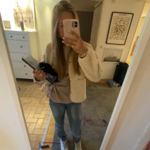 Beige teddyjacka - Mysig beige teddyjacka med knappar framtill. Perfekt för kyliga dagar med sin fluffiga och varma design. Jackan har långa ärmar och en rund halsringning.