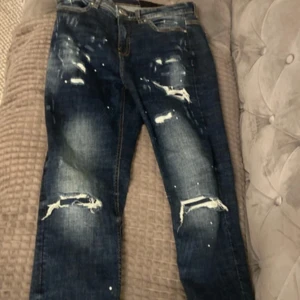 Blå jeans från Supply & Demand - Snygga blå jeans med slitna detaljer och färgstänk från Supply & Demand. De har en klassisk femficksdesign och en bekväm passform. Perfekta för en avslappnad stil.