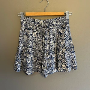 Blommig kjol med inbyggda shorts  - Snygg och bekväm kjol med inbyggda shorts, blommigt mönster i blått och vitt. De har ett knytband i midjan för justerbar passform. 💗