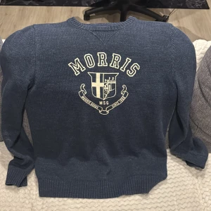 Blå tröja från Morris - Säljer en snygg blå tröja från Morris med ett stort tryck på framsidan. Tröjan har långa ärmar och ribbade muddar vid ärmslut och nederkant. Perfekt för en stilren look. Köptes för 4500 kronor. Inte använd så mycket