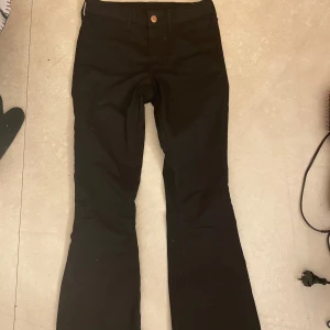 Svarta bootcut byxor - Snygga svarta bootcut byxor med mellan hög midja och knappdetalj. Perfekta för en stilren look.