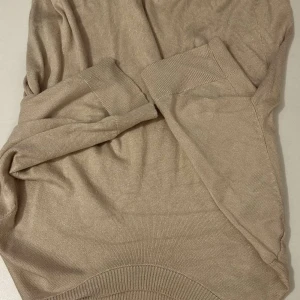 Beige tröja från 157 - Säljer en stilren beige tröja från 157. Tröjan har korta ärmar och är tillverkad i ett mjukt material med ribbade muddar vid ärmslut och nederkant. Perfekt för en avslappnad look.