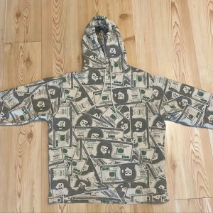 Mönstrad hoodie från Ripndip - Cool hoodie från Ripndip med ett unikt mönster av sedlar i grönt och grått. Tröjan har en klassisk passform med huva och långa ärmar. Perfekt för dig som vill sticka ut med en annorlunda stil.