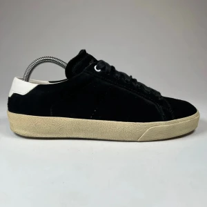  Saint Laurent - Snygga svarta sneakers i mocka från Saint Laurent med vit häl och beige sula. Skorna har klassisk snörning och en stilren design som passar perfekt för en trendig look.