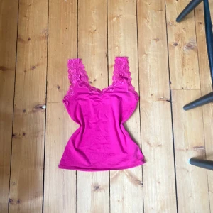 Rosa linne med spetsdetaljer - Säljer ett snyggt rosa linne med spetsdetaljer vid axelbanden och halsringningen. Perfekt för att lägga till en touch till din outfit. Passar bra till både jeans och kjol. Fint skick!