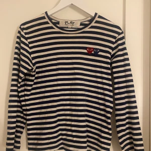 Randig tröja från Comme des Garçons - Säljer en randig tröja från Comme des Garçons i marinblått och vitt. Tröjan har långa ärmar och två broderade hjärtan på bröstet i rött och blått. Storlek s, tröjan är för män men funkar lika bra för kvinnor. Tröjan är oanvänd och original priset är runt 2000kr