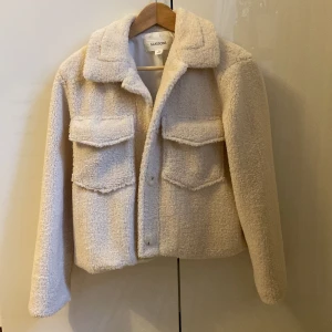 Beige teddyjacka från Glassons - Mysig beige teddyjacka från Glassons med två stora fickor framtill. Jackan har en klassisk krage och stängs med knappar. Storlek S. Ny skick, ej använt. 