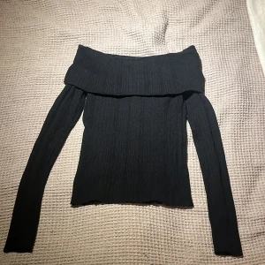 Svart offshoulder tröja - Snygg svart offshoulder tröja med ribbad design. Perfekt för en stilren look. Tröjan har långa ärmar och en bekväm passform.