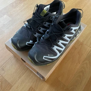 Svarta Salomon sneakers med Gore-Tex - Säljer ett par svarta Salomon sneakers med Gore-Tex teknologi. Skorna har en robust sula med bra grepp och snörning för optimal passform. Perfekta för utomhusaktiviteter och håller fötterna torra i alla väder.