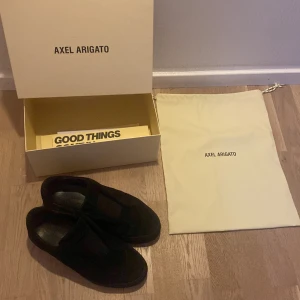 Svarta sneakers från Axel Arigato - Snygga svarta sneakers från Axel Arigato i mocka. Skorna har en stilren design utan snörning och en diskret logga på sidan. Perfekta för en minimalistisk look. Priset går att diskutera!!