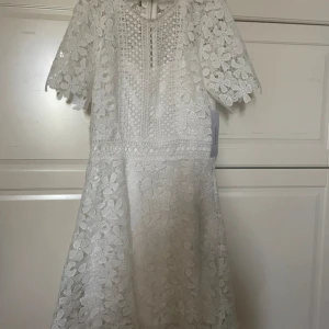 Vit spetsklänning från Bubbleroom - Säljer en elegant vit spetsklänning från Bubbleroom. Klänningen har korta ärmar och ett vackert blommigt mönster. Perfekt för sommarens festligheter med sin fina passform och detaljerade spets. NY MED PRISLAPP