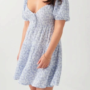 Blommig blå klänning - Charmig blå klänning med vita blommor och kort puffärm. Den har en söt knytning framtill och en luftig kjol. Perfekt till sommarn. Använd 2ggr. Säljer pga inte min stil, köpte för 399kr men pris kan diskuteras ☺️