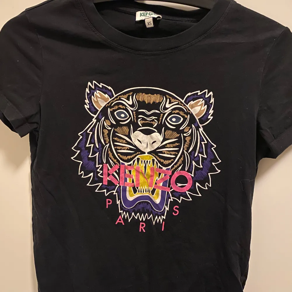 Säljer en snygg svart t-shirt från Kenzo med ett coolt tigertryck i flera färger på framsidan. T-shirten är kortärmad och har en normal passform. Perfekt för att ge din outfit en edgy touch!. T-shirts.