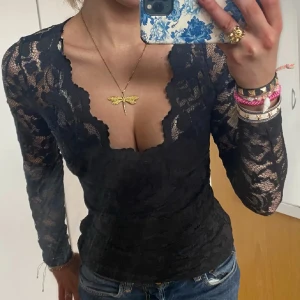 Svart spetsblus - Säljer en elegant svart spetsblus med långärmad design. Blusen har en v-ringad stil och är tight passande, perfekt för festliga tillfällen. Den har ett litet hål vid armen men som är ihopsytt❤️