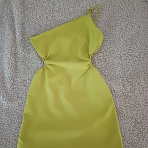Gul oneshoulder klänning - Säljer en snygg gul-grön oneshoulder klänning. Perfekt för sommarens fester! Klänningen har en tight passform som framhäver figuren.