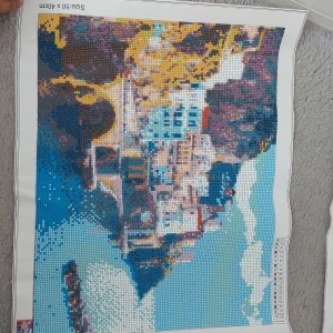 Diamanttavla med kustmotiv - En färgglad och detaljerad diamantmålning som föreställer en kuststad med klippor och hav. Tavlan har en blandning av blå, gula och bruna nyanser som skapar en livfull och harmonisk bild. Storleken är 50x40 cm, vilket gör den perfekt.