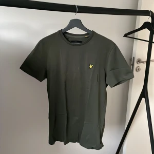 Grön t-shirt från Lyle & Scott - Säljer en snygg mörk grön t-shirt från Lyle & Scott i storlek M. T-shirten är kortärmad och gjord i mjukt bomullsmaterial. Passar perfekt till både jeans och shorts!