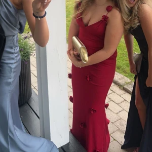 Röd långklänning med blommor - Elegant röd långklänning med blommiga detaljer. Klänningen har smala axelband och en figurnära passform, perfekt för bal ❤️ Säljer pga att jag ej kommer få användning för den!! 