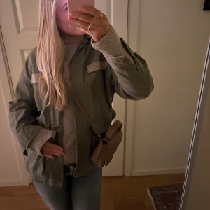 Grön jacka från Zara - Säljer en snygg grön jacka från Zara med långa ärmar och knappar framtill. Jackan har dekorativa detaljer på bröstfickorna och en klassisk krage. Perfekt för en stilren look.