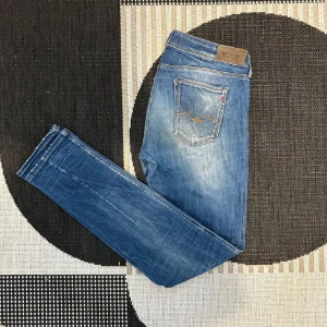 Blå jeans från Replay - Snygga blå jeans från Replay med en klassisk femficksdesign och lätt slitna detaljer. Perfekta för en avslappnad stil. Märkeslappen syns tydligt på baksidan.