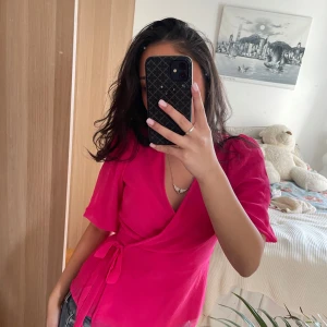 Rosa omlottopp - Säljer en snygg rosa omlottopp med knytband i midjan. Toppen har korta ärmar och en v-ringad design som ger en stilren look. Perfekt för tjejmiddagar eller till sommaren 🥰🥰Från Vera Moda, jag brukar ha 36 💕