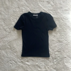 Svart ribbad t-shirt från Zara - Säljer en stilren svart ribbad t-shirt från Zara. Perfekt basplagg med korta ärmar och rund halsringning. Passar till alla tillfällen och är lätt att matcha med andra plagg. 🖤