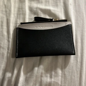 Svart och vit plånbok med dragkedja - Snygg och praktisk svart plånbok med vita detaljer och dragkedja. Perfekt för att hålla ordning på kort och kontanter. Har flera kortfack och en transparent ficka för ID eller foto.