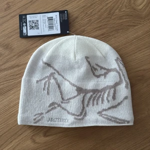 Vit mössa från Arc'teryx - Snygg vit mössa från Arc'teryx med ett stilrent fågelmönster i grått. Perfekt för kyliga dagar med sin mjuka och bekväma passform. Tillverkad i högkvalitativt material för extra värme och komfort. Helt ny, säljer då jag inte skickade tillbaka i tid. Samma pris som på hemsidan. 
