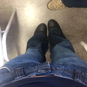 Mörkblå bootcut jeans - Snygga mörkblå bootcut jeans med klassisk femficksdesign och knappgylf. Perfekta för en avslappnad stil med en touch av retro. Köpta second hand och pris kan diskuteras