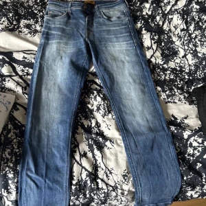 Jack and Jones jeans  - Snygga blå jeansbyxor med en klassisk straight fit. De har en knappgylf och är i storlek w32. Perfekta för en avslappnad stil.