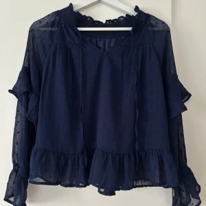 Marinblå blus med volanger - En marinblå blus med V-ringning samt knytning 💞Blusen har dubbelt tyg både fram och bak, medan ärmarna har ett genomskinligt tyg med en volang ☺️Endast testat!