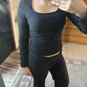 Svart ribbad topp - Säljer en stilren svart ribbad topp med lång ärm och en croppad passform. Perfekt för en trendig look. Passar bra till både jeans och kjol.