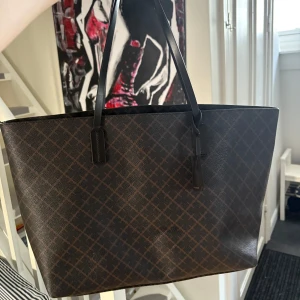 Brun väska från By Malene Birger - Snygg brun shoppingväska med rutigt mönster från By Malene Birger. Väskan har långa handtag och en praktisk hake inuti för säker förvaring. Perfekt för att bära med sig allt man behöver under dagen. Köptes för 2800 original påse finns kvar.