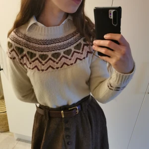 Vit stickad tröja med mönster - Säljer en mysig vit stickad tröja med ett vackert mönster i brunt, grönt och rosa runt halsen och ärmsluten. Tröjan har långa ärmar och ribbstickade muddar. Perfekt för kyliga dagar! Längd: 65cm. Armlängd: 64cm. Bredd: 48cm