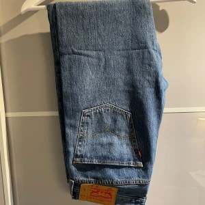 Levis 501 jeans - Klassiska Levis 501 jeans i blå denim. Dessa jeans har en rak passform och är tillverkade i slitstarkt jeanstyg. Perfekta för en tidlös stil.