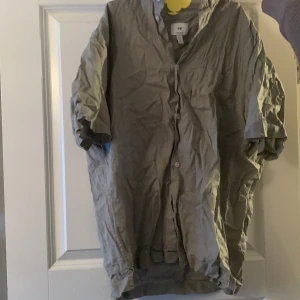 Grön skjorta från H&M - Säljer en grön skjorta från H&M i regular fit. Skjortan har korta ärmar och knappar framtill. Perfekt för en avslappnad stil. Surfer vibe 