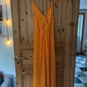 Orange prickig långklänning - Säljer en superfin orange långklänning med vita prickar. Klänningen har smala axelband och en v-ringad design som ger en somrig känsla. Perfekt för varma dagar och ger en härlig färgklick till garderoben. 🌼