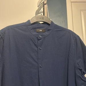 Mörkblå skjorta från C&A - Snygg mörkblå skjorta från C&A med en stilren design. Skjortan har en henley-krage och knappar framtill. Perfekt för en avslappnad men ändå uppklädd look.