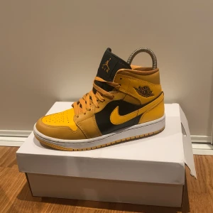 Nike Air Jordans i gult och svart - Snygga Nike Air Jordans i en fräsch gul och svart färgkombination. Skorna har en klassisk hög design med snörning och den ikoniska Air Jordan-loggan på sidan. Perfekta för att sticka ut i mängden!