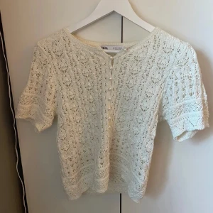 Vit spetsblus från Zara - Säljer en söt vit spetsblus från Zara med korta ärmar och knappar framtill. Perfekt för en somrig look med sitt luftiga och eleganta mönster. Blusen har en fin struktur och är lätt att matcha med olika outfits. Använt få ggr så nyskick.