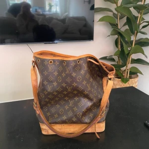  NOÉ från Louis Vuitton - Säljer en klassisk brun axelväska från Louis Vuitton med det ikoniska monogrammönstret. Väskan har justerbara axelremmar och detaljer i läder❤️Finns tecken på användning.
