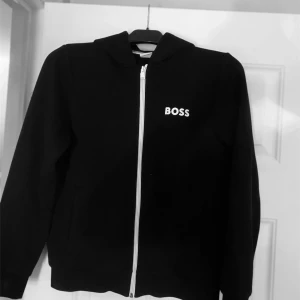 Svart hoodie från BOSS - Säljer en stilren svart hoodie från BOSS med dragkedja framtill. Tröjan har långa ärmar och en klassisk huva. Pris kan diskuteras 