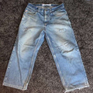 Blå jeans med slitna detaljer - Säljer ett par blå jeans med en avslappnad passform och slitna detaljer. Byxorna har en klassisk femficksdesign och råa kanter vid bensluten för en trendig look. Perfekta för en casual stil. OBS: ACCEPTERA INTE TILLBAKA SKICKNINGAR