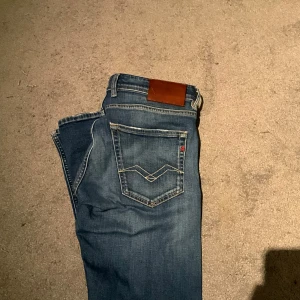 Blå jeans från Replay - Snygga blå jeans från Replay med klassisk femficksdesign och en läderdetalj vid midjan. Perfekta för en avslappnad stil. De har en rak passform och är tillverkade i slitstarkt denim.