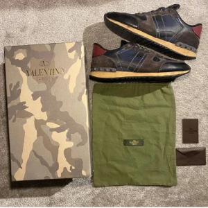 Valentino Rockrunner sneakers - Snygga Valentino Rockrunner sneakers i en mix av mocka och skinn. Skorna har en mörk färgpalett med inslag av svart och brunt samt en unik camouflagemönstrad låda. Perfekta för en stilren look. Defekter längst fram vilket är varför det låga priset