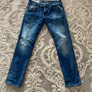 Blå jeansbyxor från Replay - Snygga blå jeansbyxor från Replay i modellen Anbass. De har en klassisk femficksdesign med en knapp och dragkedja framtill. Jeansen har en slim passform och är tillverkade i ett stretchigt material för extra komfort.